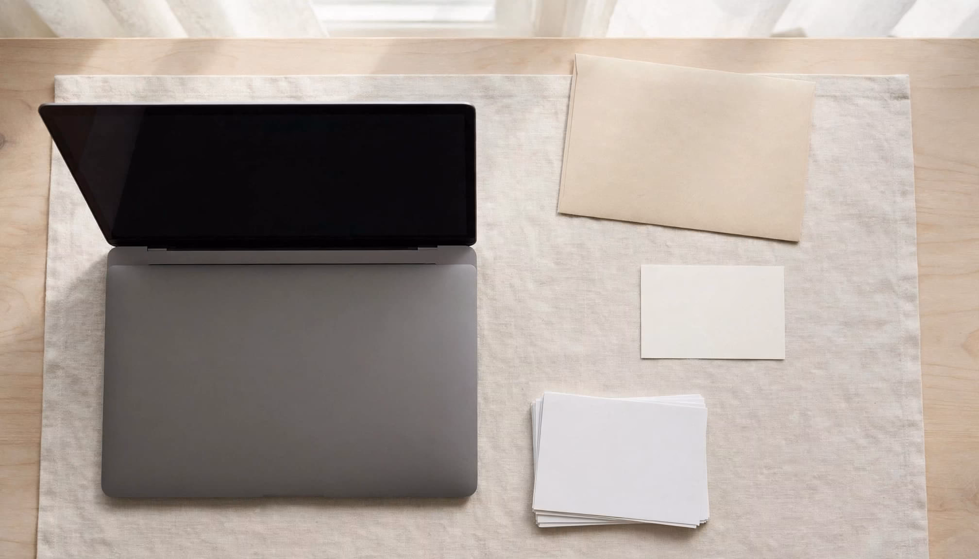 An overhead view of a laptop, an envelope, and blank cards on a cloth surface.